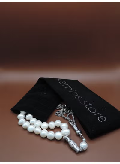 Pearl necklace with silver clasp on a black box labeled 'Kamins Store' against a brown background